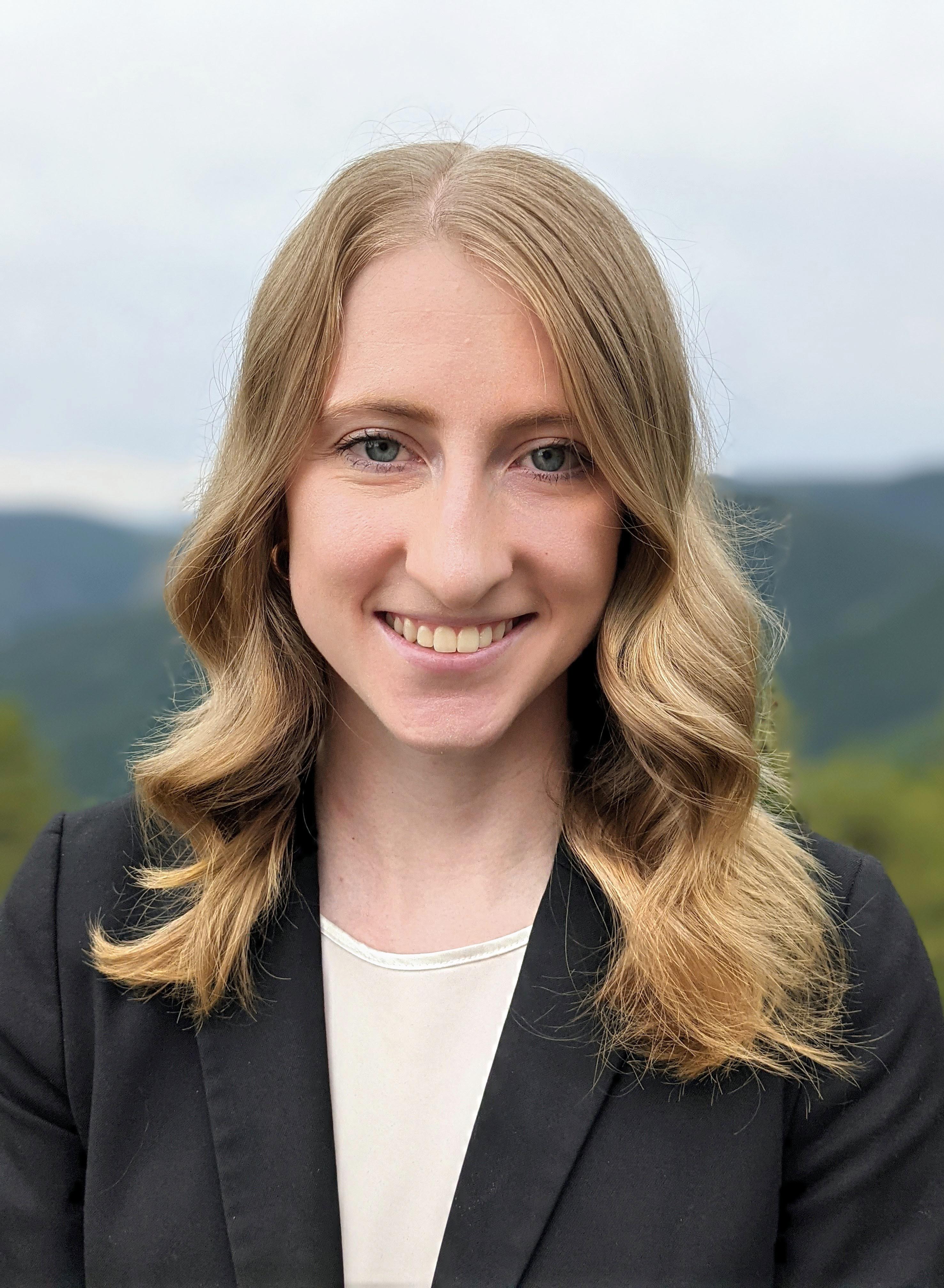 White woman wearing black blazer with mountains in background.
