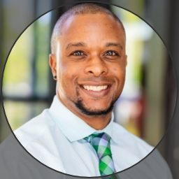 Black man with goatee in a blue collared shirt with tie